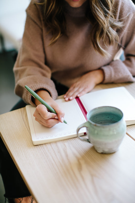 writing calligraphy in a journal with a mug nearby